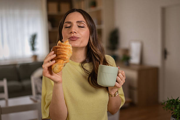Woman enjoying croissant and coffee for breakfast at home