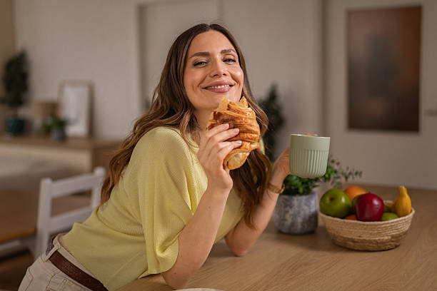 Smiling woman holding croissant and coffee mug for breakfast