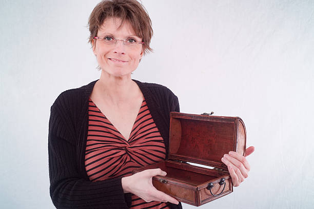 Portrait of a smiling woman holding an open wooden box against a light background.