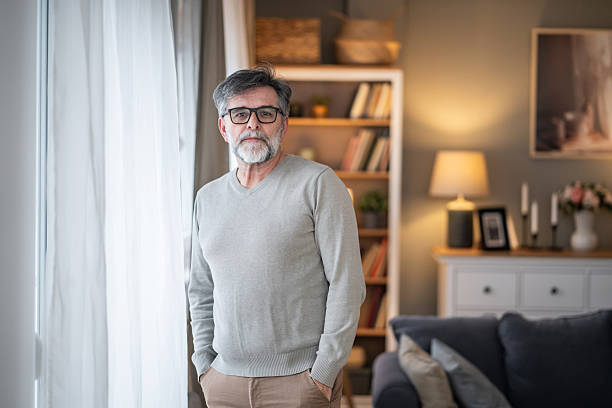 Senior man standing casually by a window in his home looking at the camera