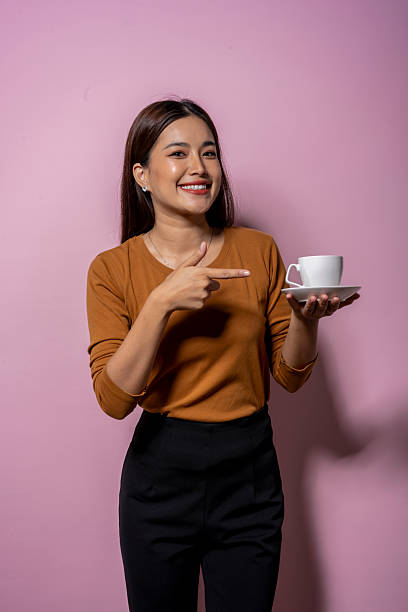 Smiling woman pointing at coffee cup on pink background