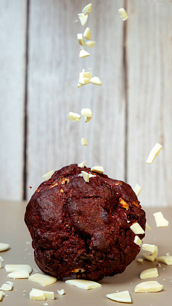 Chocolate muffin with white chocolate chips falling onto wooden background