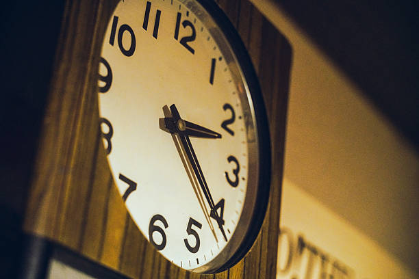 Classic round wall clock with Arabic numerals mounted on a wooden surface, illuminated by warm ambient light. Ideal for time management, nostalgia, and interior design concepts.