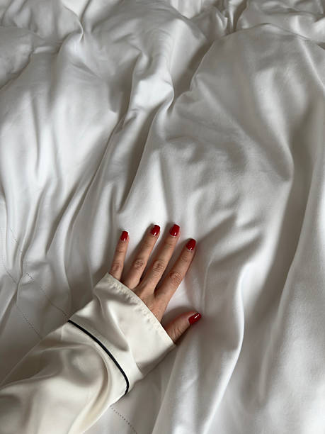 Personal perspective of woman hand touching white bed sheets in cozy bedroom