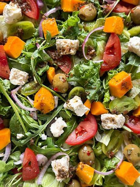 Full frame image of feta cheese mixed salad with lettuce and rocket leaves, red onion slices, mango fruit cubes, tomato quarters, green cherry tomato halves, green olives, vibrant fruit and vegetable salad background, elevated view, healthy eating concept