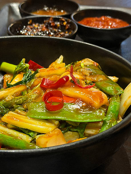 Image of colorful thai mixed vegetable stir-fry with peppers, broccoli, sugar snap peas, French beans, onions, and red chilies, vibrant asian dish
