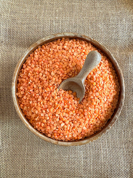 Top view of red lentils filled in a rustic wooden bowl placed over textured burlap fabric. The natural plant based ingredient represents healthy nutrition, vegetarian cooking and sustainable food culture, making it ideal for organic food campaigns, vegan recipes, agricultural concepts and clean eating promotions with earthy background and copy space.