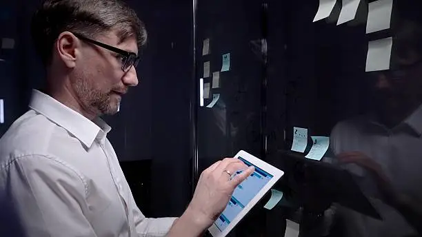 Photo of Business professional analyzing data on a tablet and planning strategy with adhesive notes on a glass board, brainstorming and organizing ideas for project development in a modern office