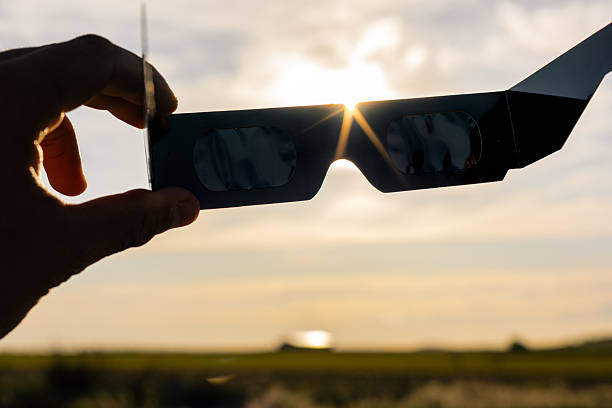 hand holding protective solar eclipse glasses, looking up at the bright sun during a celestial event for eye protection - güneş tutulması stok fotoğraflar ve resimler