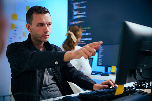 Thoughtful software developer looking at computer screen Focused male programmer sits at workstation, contemplating technical challenge. Thoughtful expression highlights concentration required for complex software development and coding in modern IT office. Best Software Life Sciences company stock pictures, royalty-free photos & images