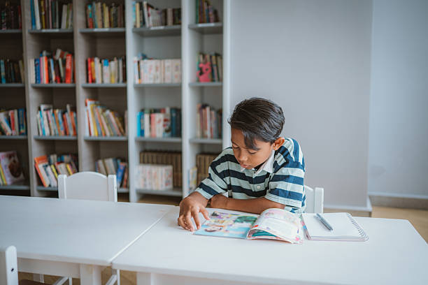 Young Asian Boy Reading Book in Library Setting stock photo