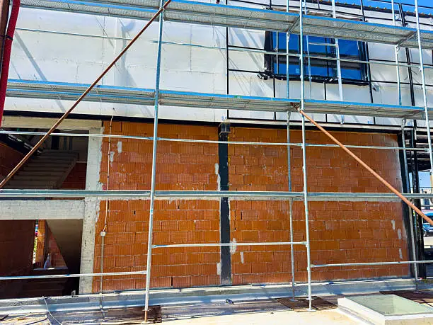 Photo of Construction work is in progress on a building with a focus on scaffolding and brick wall at a site during a sunny day