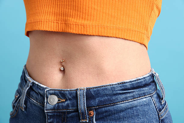 mulher com piercing no umbigo sobre fundo azul claro, close-up - model without a belly button pictures - fotografias e filmes do acervo