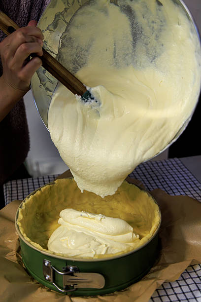 Pouring thick creamy cheesecake batter into a prepared springform pan Pouring thick creamy cheesecake batter into a prepared springform pan