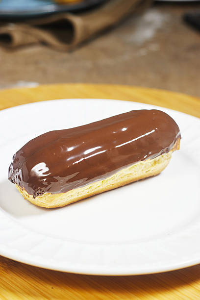 Chocolate Glazed Éclair On Plate With More Pastries In Soft Focus Background Chocolate Glazed Éclair On Plate With More Pastries In Soft Focus Background