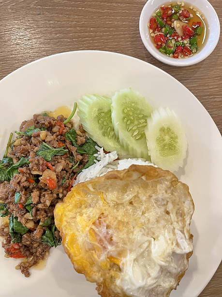 Stir fried minced beef basil rice fried egg cucumber chili sauce white rice basil leaf savory street food lunch plate Stir fried minced beef basil rice fried egg cucumber chili sauce white rice basil leaf savory street food lunch plate
