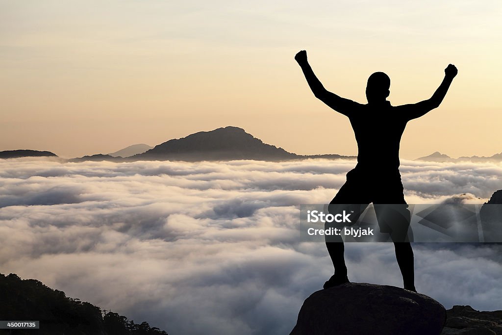 Man hiking climbing silhouette in mountains Man hiking silhouette in mountains, sunset and clouds. Male climber hiker arms outstretched on top of mountain after success climbing looking at beautiful sunset sky night landscape. Arms Outstretched Stock Photo