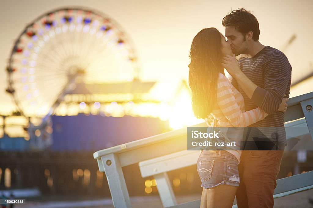 romantic couple kissing at sunset photo of a romantic couple kissing at sunset in front of santa monica ferris wheel. Amusement Park Stock Photo