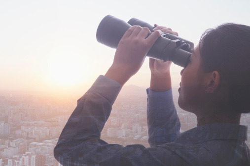 Double exposure of young businesswoman holding binoculars over cityscape of Beijing