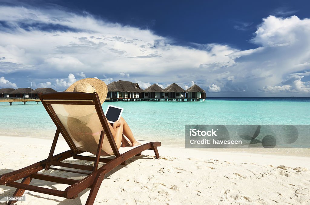 Young lady relaxing on beach lounger with her tablet Young woman in hat with tablet pc at the beach Beach Stock Photo
