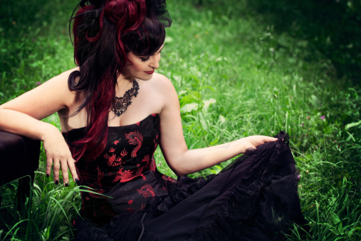 Cute goth woman in a meadow by the bench
