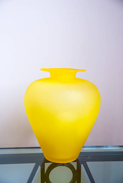 Glowing A yellow glass vase on a glass table against a wall. art deco vase stock pictures, royalty-free photos & images