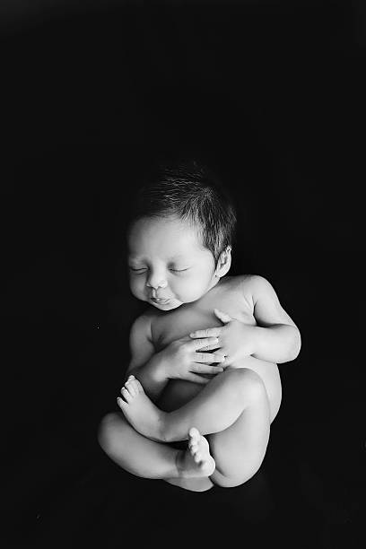 Newborn baby sleeping Newborn baby sleeping full body shot on black drop in black and white. hugging knees stock pictures, royalty-free photos & images