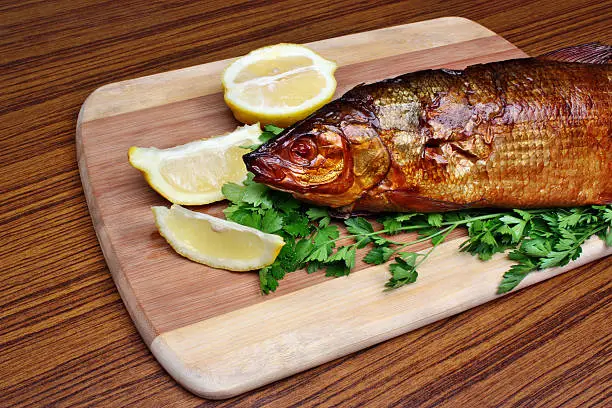 Fish smoked whitefish on a chopping board with lemon and parsley