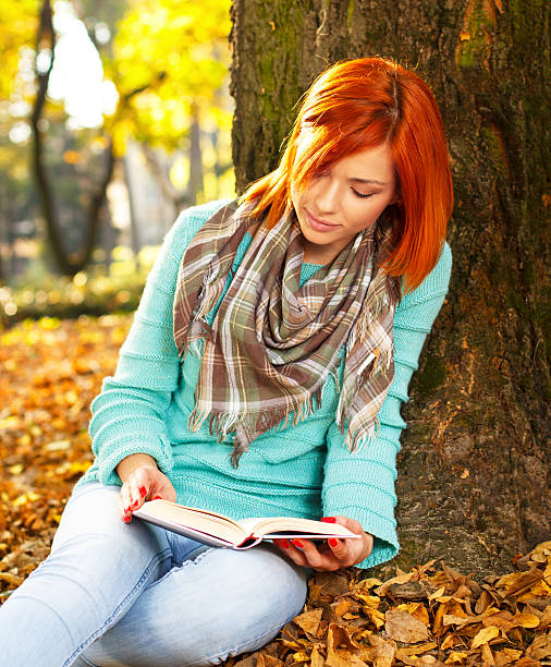 istock Young woman reading a book in nature 450266299