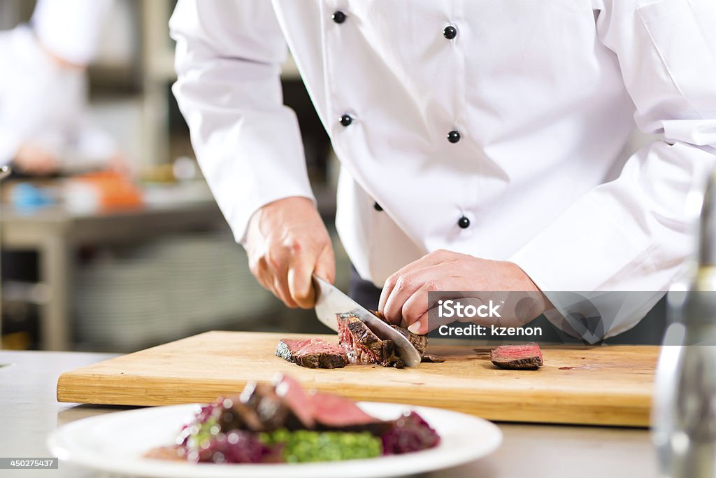 Chef in restaurant kitchen preparing food Chef in hotel or restaurant kitchen cooking, only hands, he is cutting meat or steak for a dish on plate Chef Stock Photo