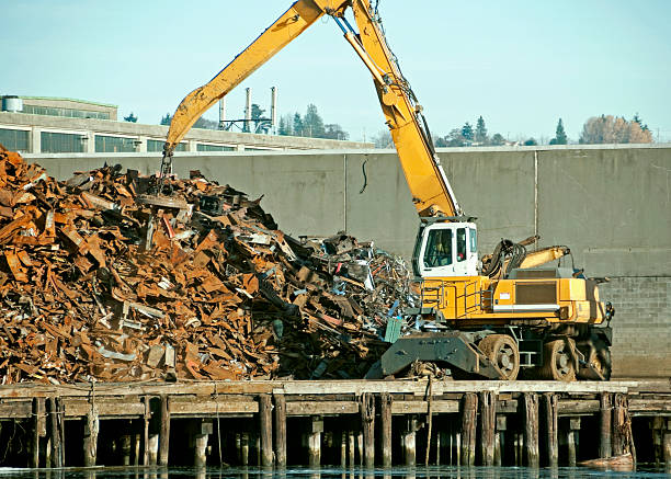 Hydraulic crane with grab attachment, loading rusty metal scrap onto a truck at the port dock. Industrial metal scrap for recycling