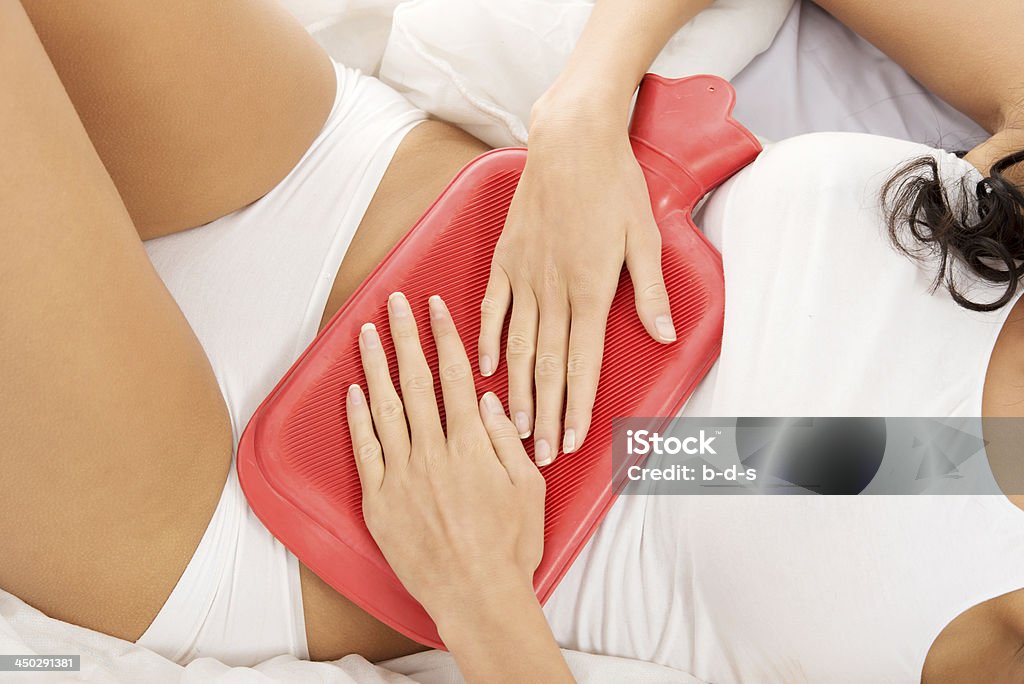 Young woman in underwear holding hot-water bag on belly. Young woman in underwear holding hot-water bag on belly. Isolated on white. Adult Stock Photo