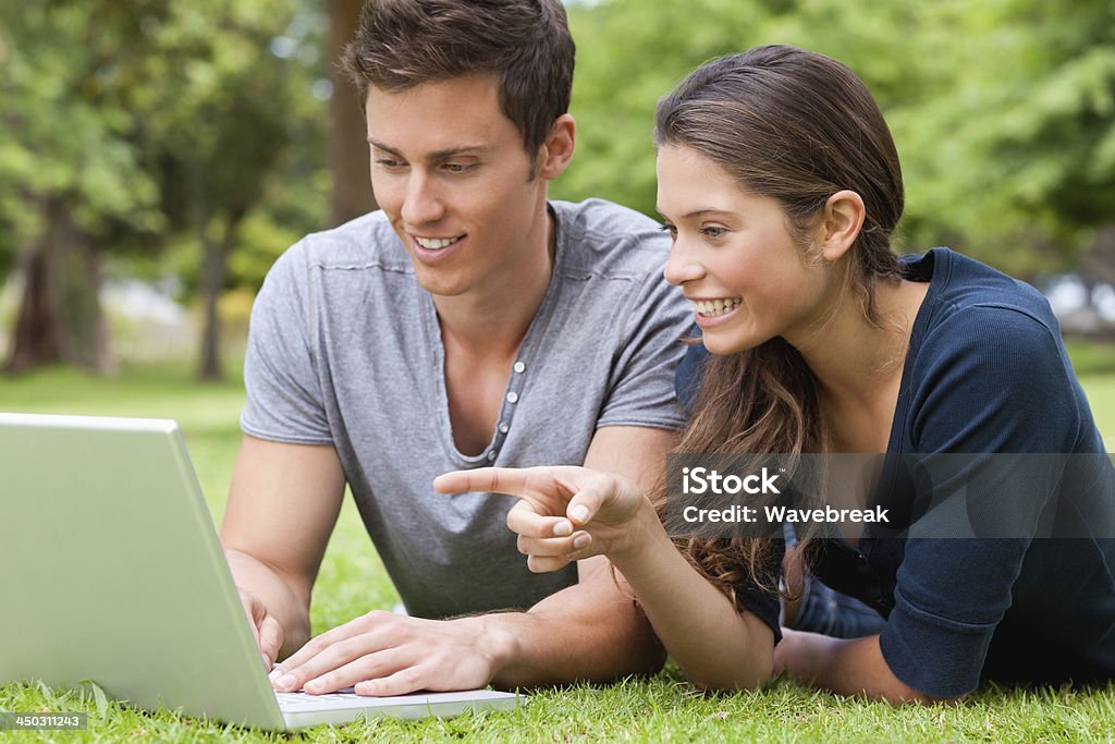 Casal usando um laptop deitado no abdômen, - Foto de stock de 18-19 Anos royalty-free