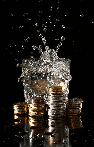istock Coins falling into a glass of water with splash 450324899