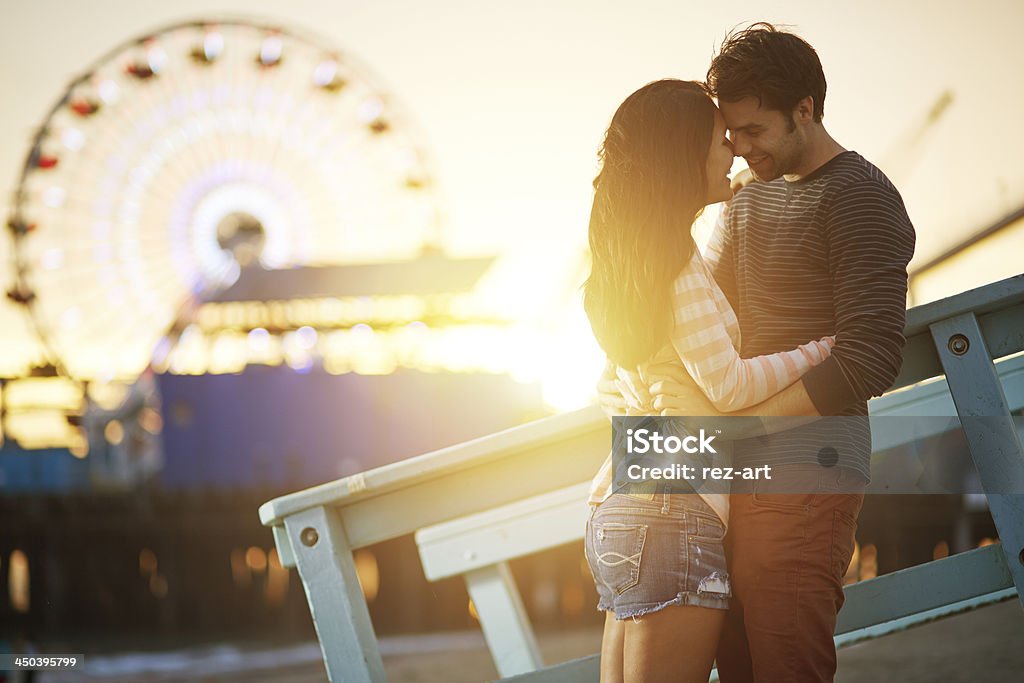 romantic couple embracing  at sunset photo of a romantic couple  embracing  at sunset in front of santa monica ferris wheel. Couple - Relationship Stock Photo