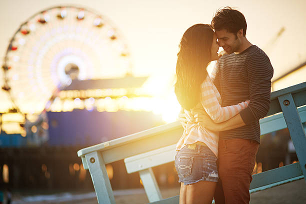 romantic couple embracing  at sunset photo of a romantic couple  embracing  at sunset in front of santa monica ferris wheel. cute couple stock pictures, royalty-free photos & images