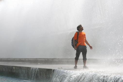 Young male person standing in fountain in spraying water