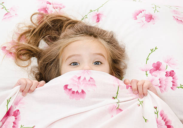 istock Young girl peeps out from floral bed covers 450419209