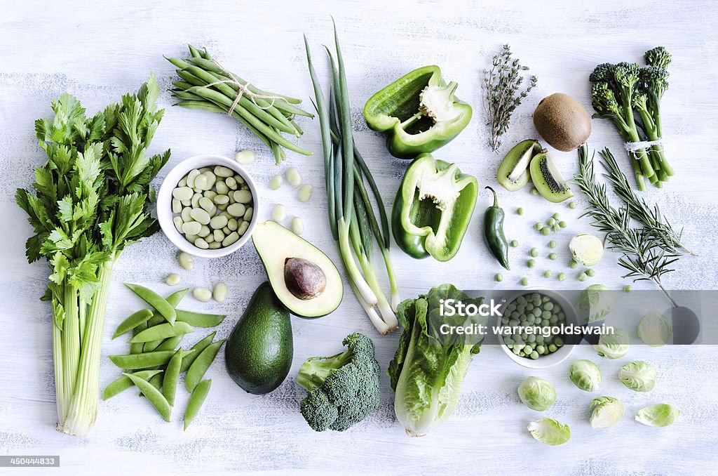 Healthy green vegetables A variety of green and leafy vegetables and fruits, of which some are cut in half.  Included in the variety of vegetables and fruits is an avocado, green bell peppers, kiwis, peas, beans and lettuce.  They are placed in a rustic white background. Vegetable Stock Photo