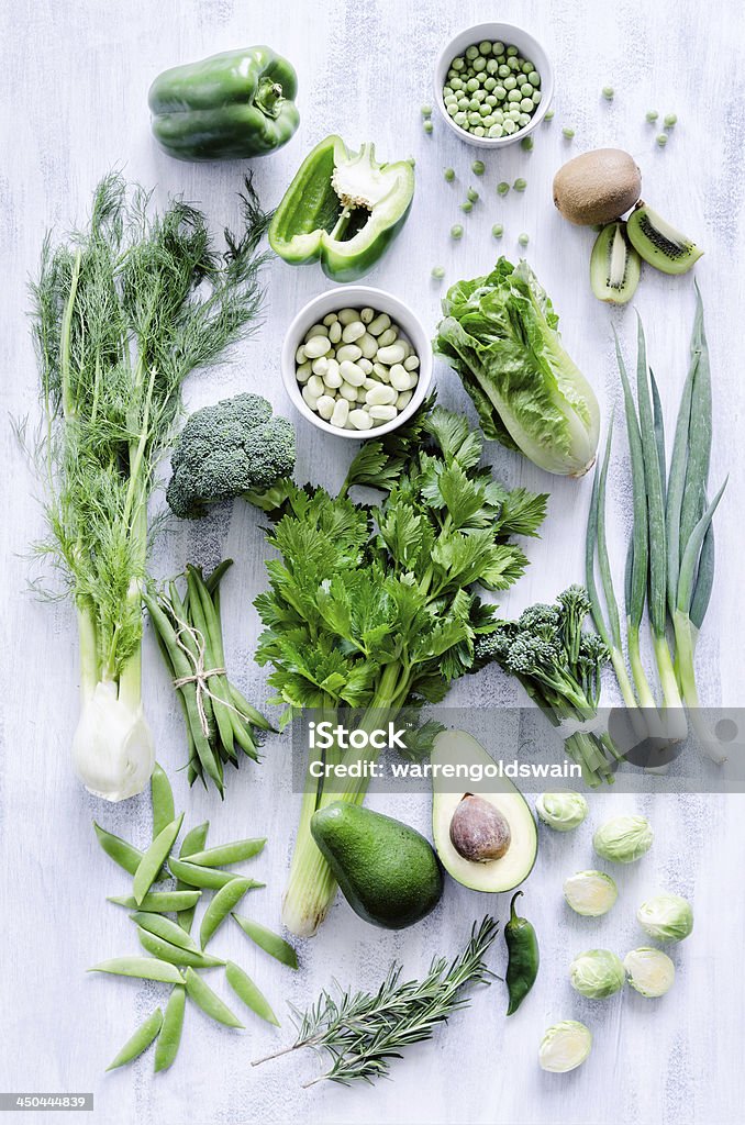 Green vegetables on white rustic background Collection of fresh green vegetables on white rustic background, broccoli, lettuce, celery, beans, capsicum, peppers, peas, brussels sprouts, kiwi, avocado, Green Color Stock Photo