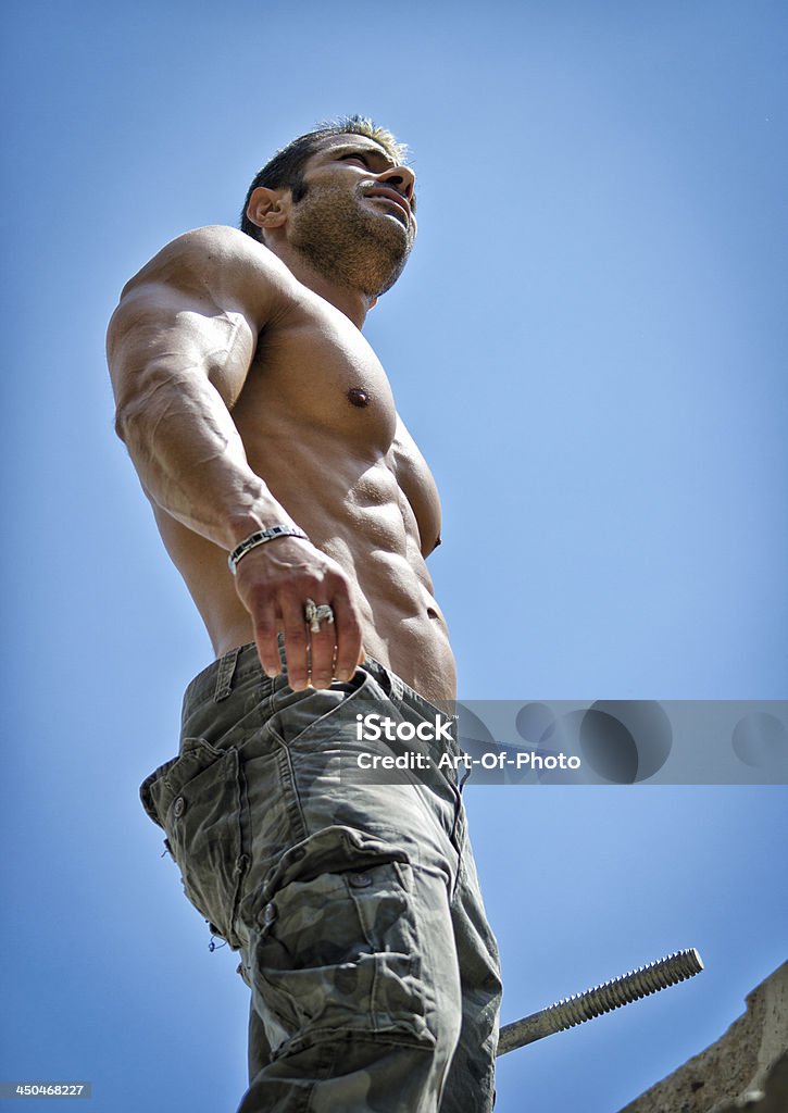 Hot, muscular construction worker shirtless seen from below Hot, shirtless, muscular construction worker shirtless seen from below against blue sky Abdominal Muscle Stock Photo
