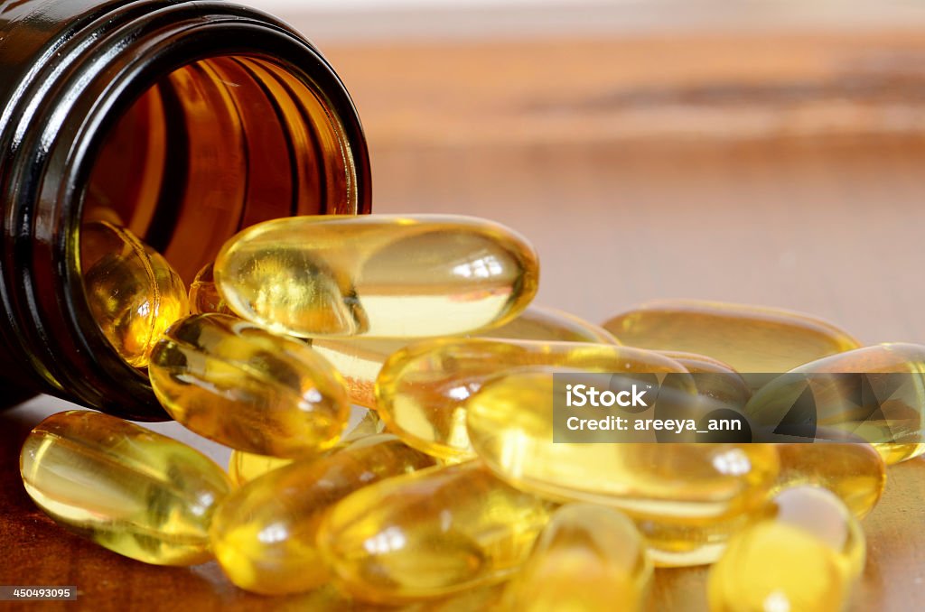 Yellow transparent capsules falling out of a brown bottle ็Heap of transparent yellow capsules pored out from amber bottle. Vitamin D Stock Photo