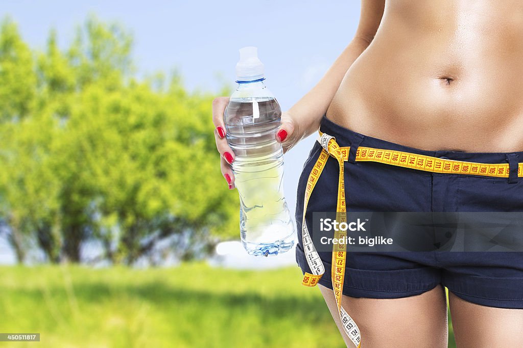 Fit healthy woman holding bottle of water Fit woman holding bottle of water wearing shorts and measuring tape against blurred nature background. Image composite. 20-24 Years Stock Photo