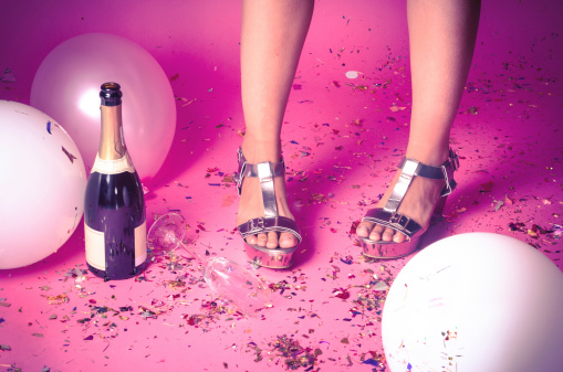 Pair of feet at a new years eve countdown party with confetti, champagne and balloons on the floor