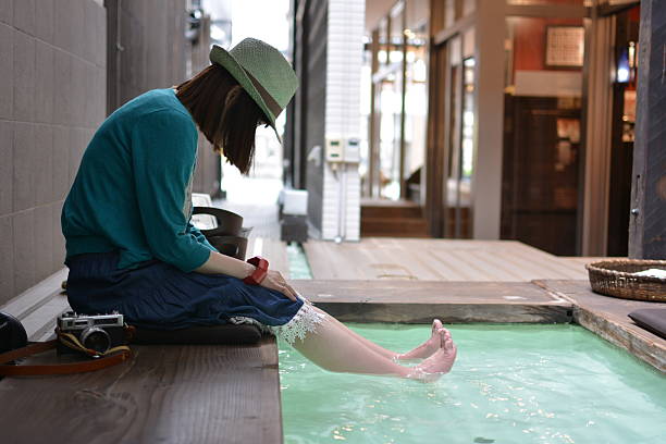 Relax woman looking at barefoot in the foot bath. Sit back woman enjoying relaxing foot bath and looking at the feet of barefoot. Woman's toes look like wrinkly prunes in water. Public foot bath. A woman wearing a straw hat. japan women human foot japanese culture stock pictures, royalty-free photos & images