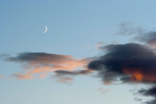 crescent of the moon with pink and dark clouds