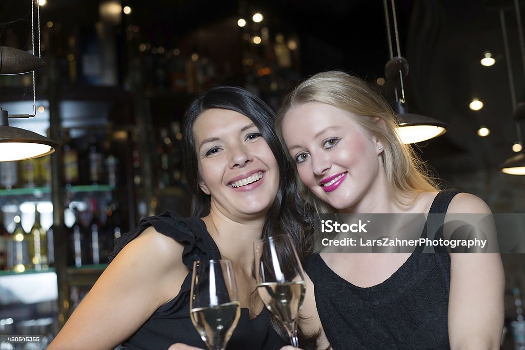 Two female friends toasting in a nightclub Two happy female good friends, one blonde and one brunette, toasting with champagne or white wine in a trendy nightclub Adult Stock Photo