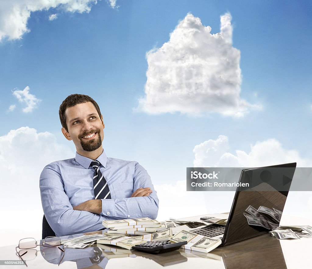 Daydreaming businessperson with arms crossed happy guy smile day dreaming with his arms crossed sitting at his desk with laptop and a lot of money Abundance Stock Photo