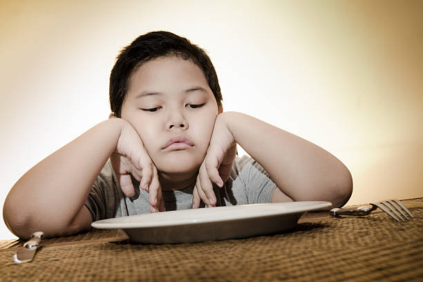 asian boy sitting sadly on dining table waiting for food