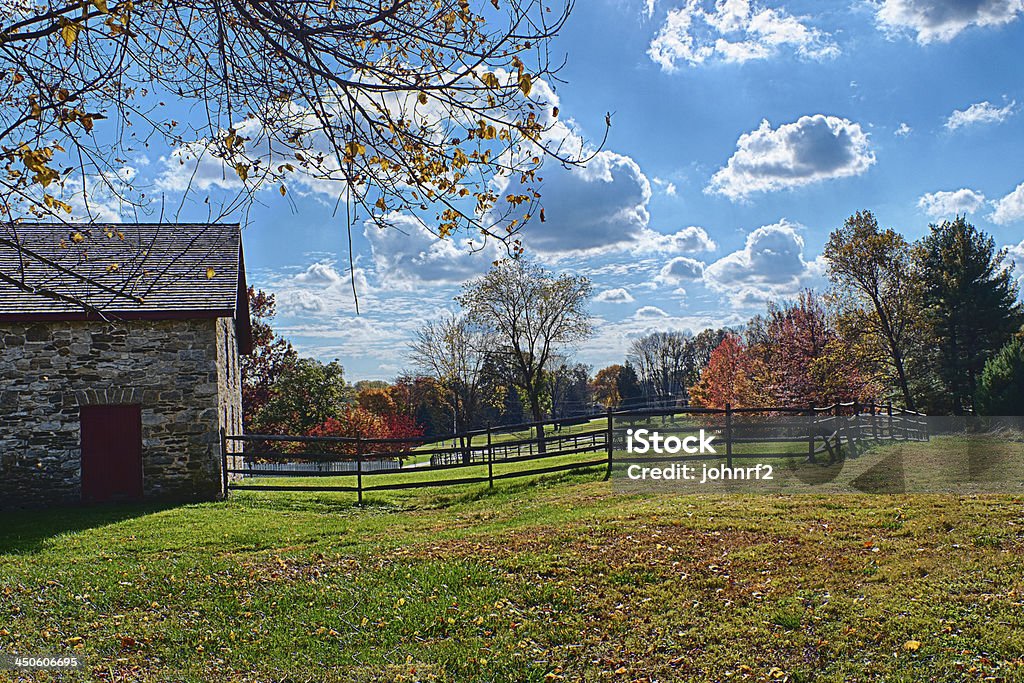 Stone Barn and Horse Corral in Autumn A hors corral with an old stone barn and split rail fence with autumn leaves and blue sky with puffy white clouds Agriculture Stock Photo